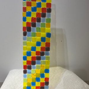 May include: A colorful glass mosaic wall art piece with a geometric pattern of squares in shades of red, yellow, blue, green, and brown.