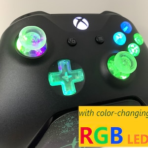 May include: Black Xbox controller with color-changing RGB LEDs on the buttons and d-pad.  The LEDs are green in this image.