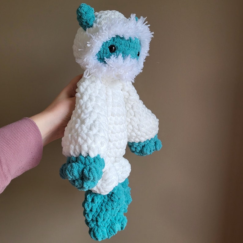May include: White crocheted plush toy with a blue and white face and blue crocheted feet. The toy is shaped like a small animal with a fluffy white mane.