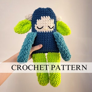 May include: Crochet pattern for a blue and green plush toy with a white face. The toy has a sleeping expression and green ears. The pattern is called "CROCHET PATTERN".