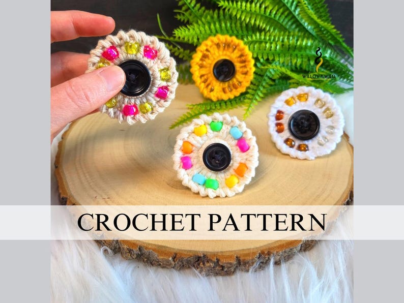 May include: Four circular crochet flower-shaped ornaments featuring a central black button and colourful beads embedded in the yarn. The crochet pieces are white, yellow, and cream-coloured, with the text CROCHET PATTERN displayed across the image.