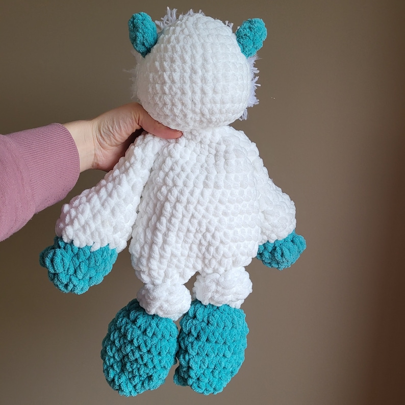 May include: White crocheted plush toy with teal blue accents. The toy has a fluffy white body with teal blue ears, arms, and feet.