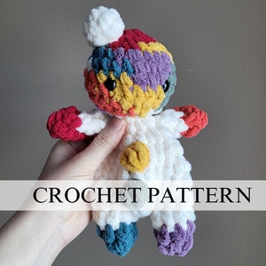 May include: A colorful crocheted stuffed animal with a white body and multi-colored arms and legs. The animal has a white pom-pom on its head and black button eyes. The animal is being held by a hand. CROCHET PATTERN is written in black text on a white background.