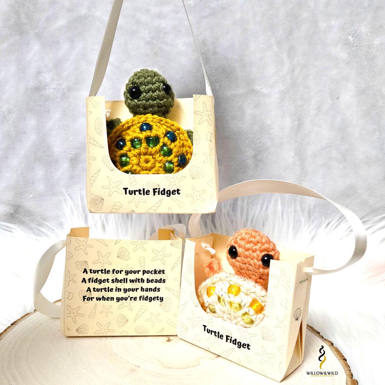 K&ouml;nnte beinhalten: Zwei geh&auml;kelte Schildkr&ouml;ten-Fidget-Spielzeuge in kleinen Geschenkboxen mit einem wei&szlig;en Schleifenbandgriff. Die Boxen sind mit einem maritimen Muster und dem Text "Turtle Fidget" verziert.