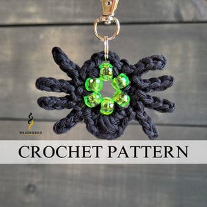 Pode incluir: Um porta-chaves de aranha em croché preto com oito pernas e um anel central de seis contas verde-lima translúcidas. A aranha está presa a um mosquetão de metal prateado. O texto "WILLOW & WILD" e "CROCHET PATTERN" está presente na imagem.