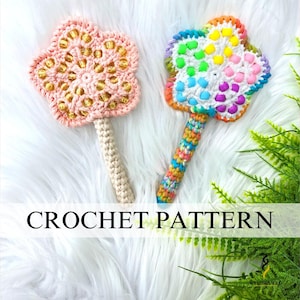 Op de afbeelding: Twee gehaakte bloemvormige items met handvatten. Eén is roze met gouden accenten, de andere is regenboogkleurig. De tekst "CROCHET PATTERN" wordt in de afbeelding weergegeven. De items staan op een witte, zachte ondergrond.