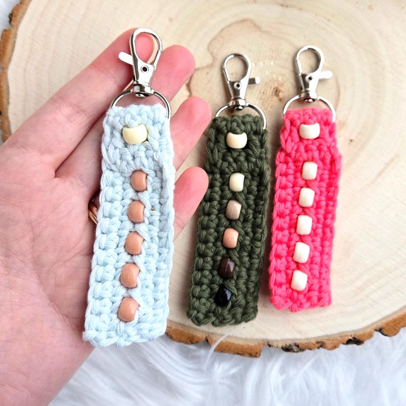 May include: Three crocheted keychains with beaded accents. The keychains are light blue, olive green, and pink. Each keychain has a silver metal ring.