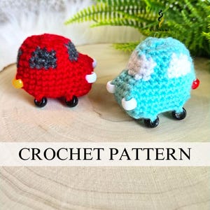 May include: Two crocheted toy cars, one red and one teal, sit on a wooden surface. The red car has gray windows and black wheels. The teal car has white and gray accents. The text "CROCHET PATTERN" is displayed below the cars.
