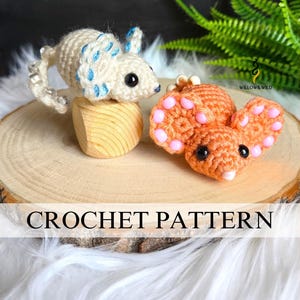 May include: Two crochet amigurumi animals: a cream-colored axolotl with blue accents and an orange mouse with pink details. The axolotl sits on a wooden block. The image includes the text "CROCHET PATTERN".