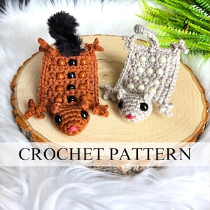 Może przedstawiać: Dwa szydełkowe stworzenia przypominające jaszczurki w kolorze brązowym i szarym, ozdobione koralikami i czarnymi oczami, spoczywają na drewnianym plastrze. Brązowa jaszczurka ma czarny, włochaty ogon. Poniżej jaszczurek widnieje napis "CROCHET PATTERN".
