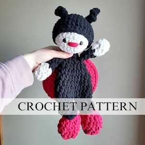 May include: Crochet pattern for a ladybug toy. The ladybug is black with red spots and white accents. The toy is being held by a hand.