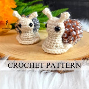 May include: Two small crocheted snail figures with cream-colored yarn bodies and black bead eyes. One snail features a shell made of metallic silver beads, while the other has a shell made of metallic copper beads. The text CROCHET PATTERN is visible.