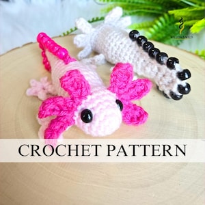 Puede incluir: Dos juguetes de axolotl de ganchillo, uno rosa y blanco, el otro blanco con detalles negros. El axolotl rosa tiene branquias de color rosa brillante y una cola a juego. El texto "CROCHET PATTERN" se muestra en una pancarta blanca.