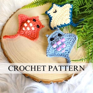 May include: Three handmade crochet stingrays in coral, blue, and cream colours. The coral ray has white accents, the blue ray has pink accents, and the cream ray has blue accents. The text "CROCHET PATTERN" is displayed on the image.
