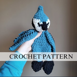 Könnte beinhalten: Häkelanleitung für ein blaues Plüschvogel-Spielzeug. Der Vogel hat eine weiße Brust und schwarze Augen. Das Spielzeug wird in einer Hand gehalten.