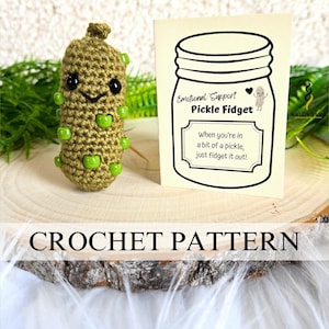May include: Crochet pattern for a green pickle-shaped fidget toy. The pattern includes instructions for making a cute pickle with a smiling face and green beads. The text on the card reads "Emotional Support Pickle Fidget. When you're in a bit of a pickle, just fidget it out!"
