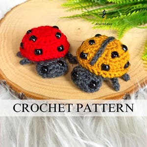 May include: Two crocheted ladybug figures, one red and one yellow, with black spots and gray bodies, sit on a wooden slice. The ladybugs are handmade. The text "CROCHET PATTERN" is displayed below the ladybugs.