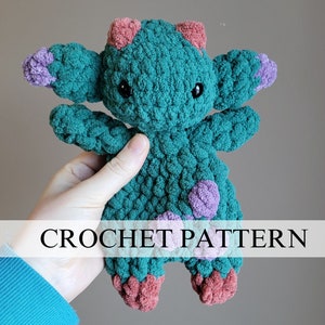 May include: Crochet pattern for a teal blue amigurumi creature with purple and pink accents. The creature has large eyes and a textured surface.