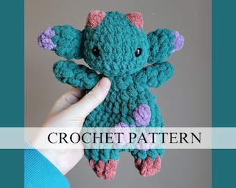 May include: Crochet pattern for a teal blue amigurumi creature with purple and pink accents. The creature has large eyes and a textured surface.