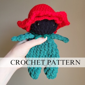 May include: Crochet pattern for a green and black doll with a red hat. The doll is holding a small green flower in its hand. The doll is wearing a green dress and a red hat. The doll is sitting on a white background. CROCHET PATTERN.