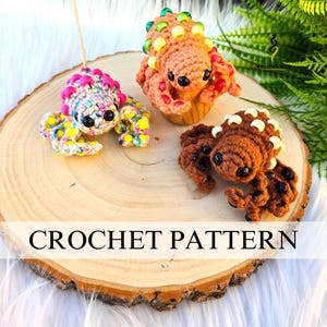 May include: Three handmade crochet creatures in vibrant colors are displayed on a wooden slice. One is multi-colored, another is orange, and the third is brown. The text "CROCHET PATTERN" is visible on the wooden slice.