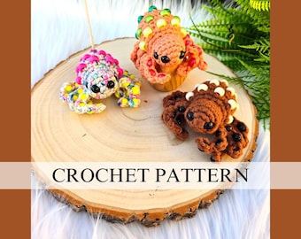 May include: Three handmade crochet creatures in vibrant colors are displayed on a wooden slice. One is multi-colored, another is orange, and the third is brown. The text "CROCHET PATTERN" is visible on the wooden slice.