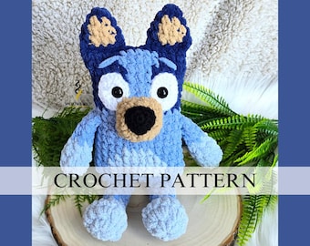 May include: Crochet pattern for a blue and brown plush dog toy. The dog has a blue and white face with black eyes and a black nose. The dog is sitting on a wooden surface.
