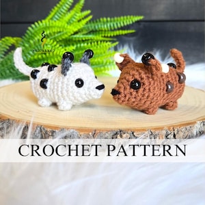 May include: Two crocheted dog figurines, one white with black spots and the other brown with lighter brown spots. The dogs are on a wooden slice with a green plant in the background. The text "CROCHET PATTERN" is displayed.
