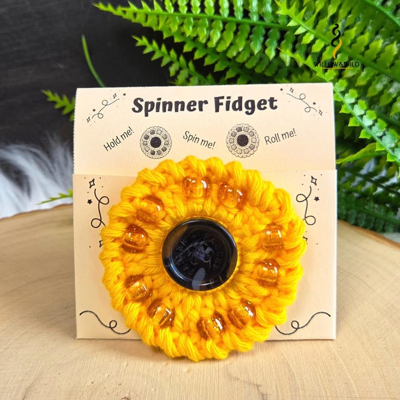 May include: A yellow crocheted spinner fidget toy with amber-coloured beads attached to a beige display card. The card features the text Spinner Fidget, Hold me!, Spin me!, and Roll me! with decorative line art and the Willow & Wild logo.