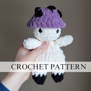 May include: Crochet pattern for a white amigurumi mushroom with a purple and black hat. The mushroom has black eyes and a black mouth. CROCHET PATTERN is written in white text on a white banner.