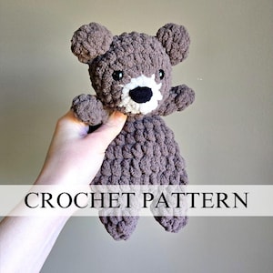 May include: A handmade crochet bear in shades of brown, with a white muzzle and black eyes. The bear has small ears and outstretched arms. The text "CROCHET PATTERN" is displayed across the bottom of the image.