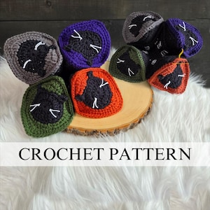 May include: A collection of crocheted cat-themed cubes in various colors including grey, purple, green, orange, and black. Each cube features a black cat face with white embroidered whiskers and eyes. The text CROCHET PATTERN is displayed at the bottom.