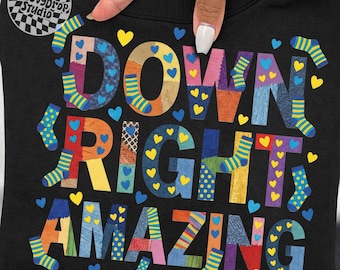 May include: Black sweatshirt with the words "DOWN RIGHT AMAZING" in colorful patchwork letters. The design includes socks and heart shapes in various colors. The GroovyDrop Studio logo is in the upper left corner.