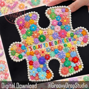 Puede incluir: Una pieza de rompecabezas bordada con flores multicolores en tonos rosa, amarillo, azul y naranja. La frase "IT'S OKAY TO BE DIFFERENT" está bordada en el centro. El contorno está adornado con perlas blancas.