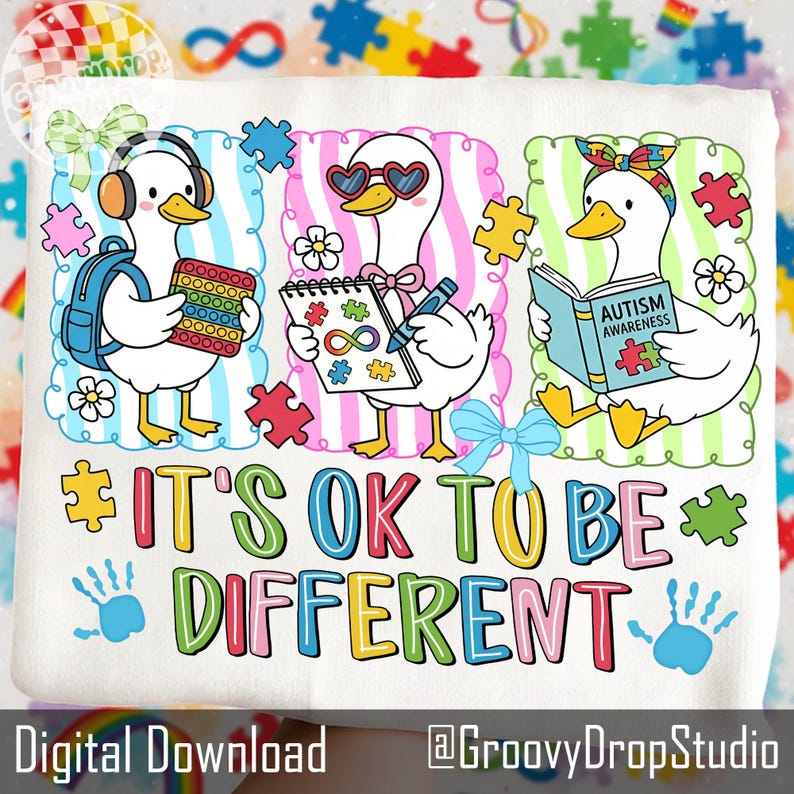 May include: White t-shirt with a colorful graphic featuring three cartoon ducks. One duck wears headphones and holds a pop-it toy, another wears heart-shaped sunglasses, and the third reads a book. The text "IT'S OK TO BE DIFFERENT" is displayed.