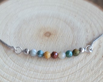 May include: A silver chain necklace with a row of colourful gemstone beads. The beads are in shades of green, brown, yellow, and red.