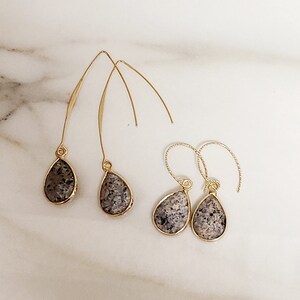 May include: A set of four gold dangle earrings with grey stone teardrop shaped pendants.