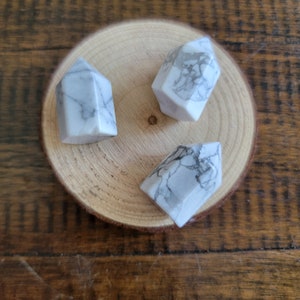 May include: Three white howlite crystal points with grey veining, arranged on a wooden surface.