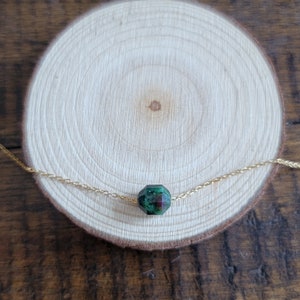 May include: A gold chain necklace with a single green and red gemstone pendant.