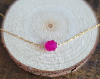 May include: A delicate gold chain necklace with a single, faceted, bright pink gemstone pendant.