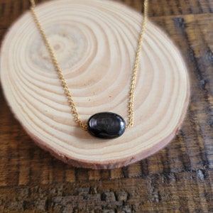 May include: A gold chain necklace with a single black oval gemstone pendant.