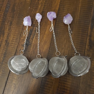 May include: Four silver tea infusers with amethyst crystal tops. Each infuser has a chain and a hook for hanging.