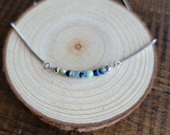 May include: A silver chain necklace with a row of blue, green, and brown gemstone beads.