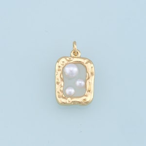 May include: A gold-colored pendant with a rectangular frame and a textured border. Inside the frame are three small, white pearls. The pendant has a loop at the top for attaching to a chain.