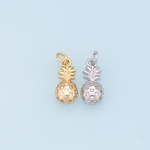 May include: Two pineapple-shaped charms, one gold-toned and one silver-toned, each adorned with small, clear crystals. The charms have a loop at the top for attaching to a necklace or bracelet. The background is a light blue.