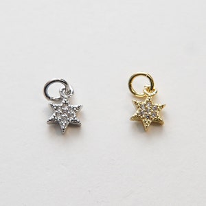May include: Two silver and gold star of David charms with clear crystal accents. The charms are on a white background.