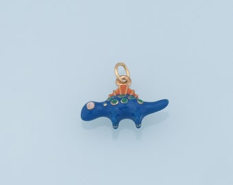 May include: A blue dinosaur charm with a gold-colored bail. The charm has green spots and an orange and gold-colored ridge along its back. The dinosaur has a small, clear gem for an eye. The charm is likely made of metal and enamel.