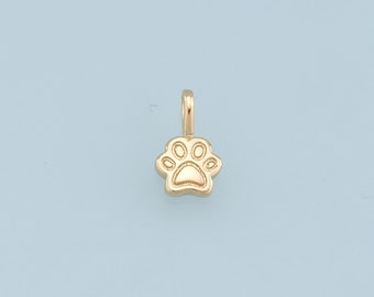 Może przedstawiać: Złoty wisiorek w kształcie łapy. Zawieszka jest mała i szczegółowa, z pętelką na górze do przymocowania do naszyjnika lub bransoletki.