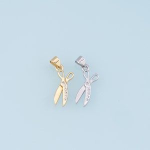 May include: Two gold and silver scissor pendants with clear crystal accents. The pendants are on a light blue background.