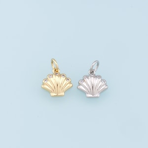 May include: Two gold and silver seashell charms with clear rhinestones. The charms are on a light blue background.